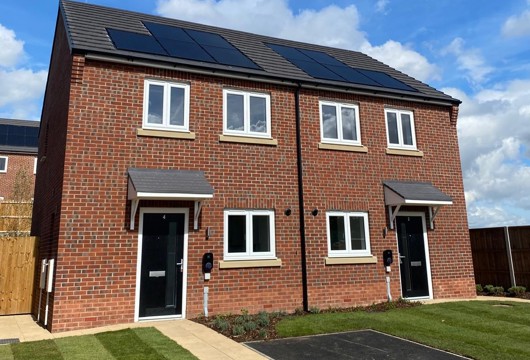 A pair of modern semi-detached houses with black front doors, white-framed windows, solar panels, and neatly maintained front gardens.