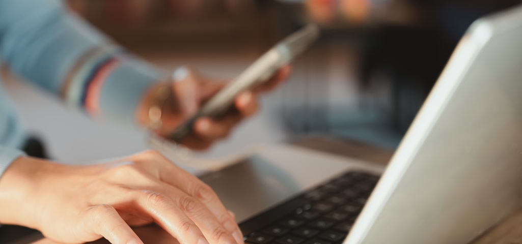 Someone in front of a laptop holding their smart phone