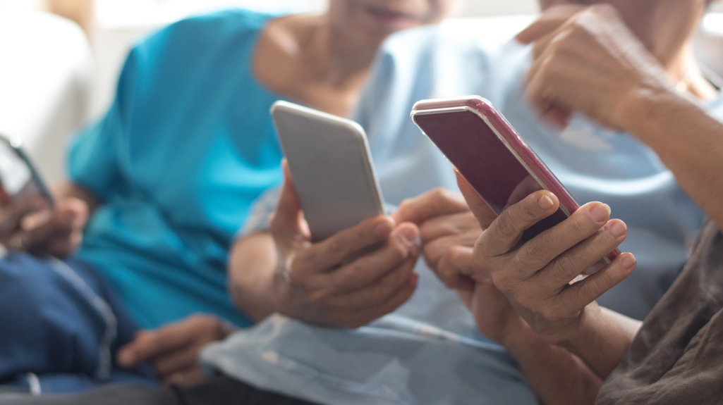 Three people sat on a sofa with mobile phones