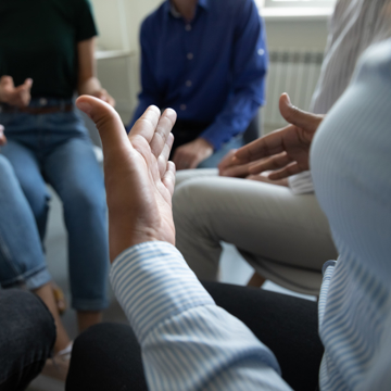 Abstract picture of people sat in a circle with one person gesturing with their hands
