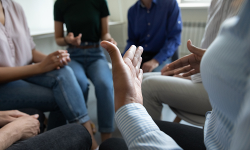 Abstract picture of people sat in a circle with one person gesturing with their hands