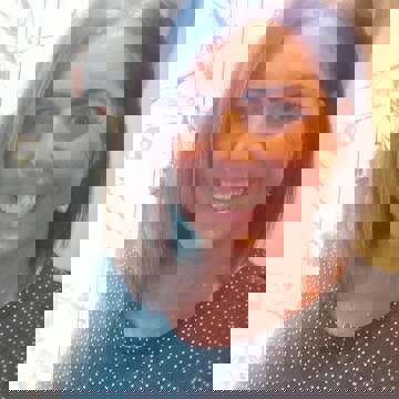 Headshot of Jodie, a woman with straight dark brown shoulder-length hair, wearing a dark teal polka dot top and a delicate silver necklace, smiling at the camera.