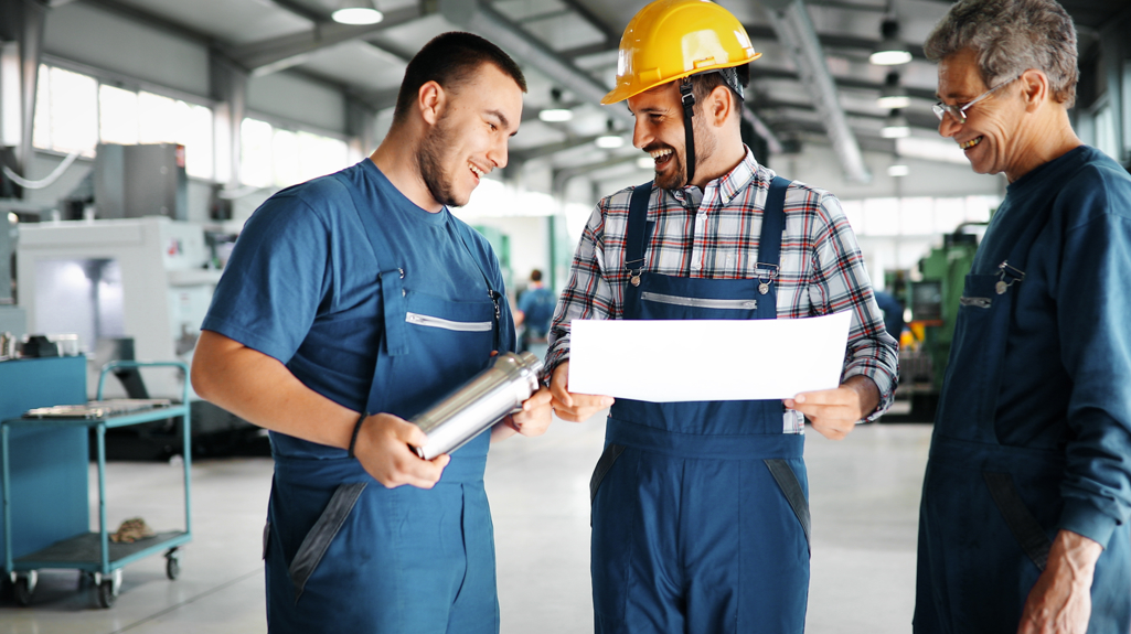 Three men stood in a warehouse wearing overalls 