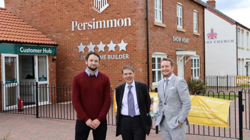 Three people stood outside a Persimmon show home smiling at the camera. 