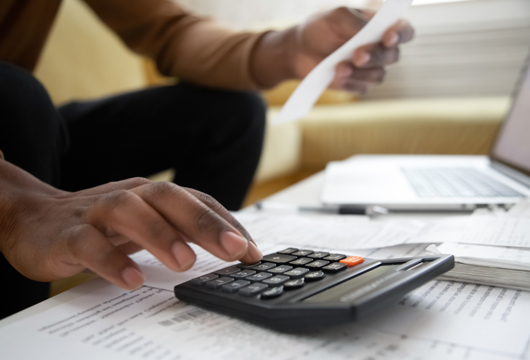 A close up shot of a hand on a calculator and holding a receipt in the other hand. 