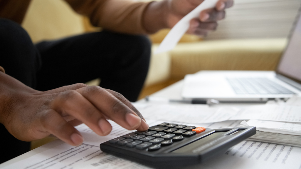 A close up shot of a hand on a calculator and holding a receipt in the other hand. 