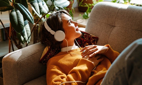 A woman laid on a sofa listening to music through headphones