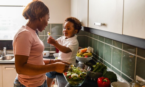 A woman cooking in the kitchen with a young child