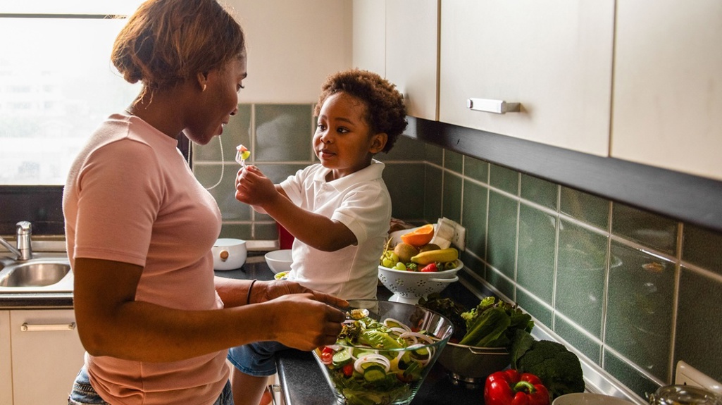 A woman cooking in the kitchen with a young child