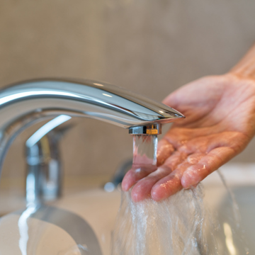 Tap running with a hand testing temperature of the water