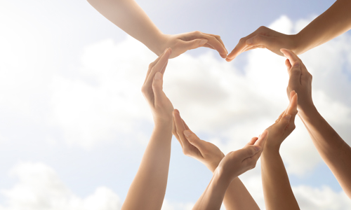 Picture of seven hands together forming the shape of a heart against the sky