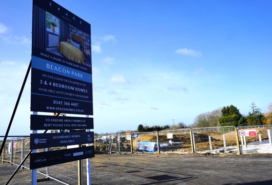 Sign for the Beacon Park housing development next to a fenced construction site under a blue sky.