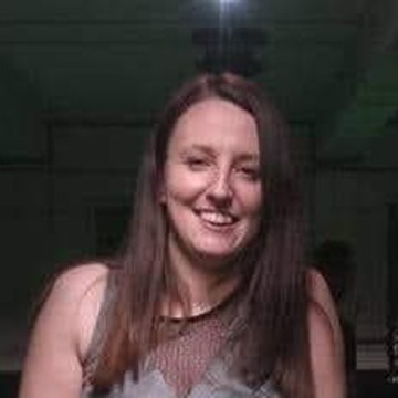 Headshot of Becky, a woman with long straight brown hair, wearing a silver/grey embellished top, smiling at the camera against a dark background