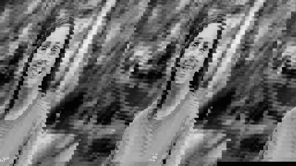 A black and white image of Leanne stood smiling at the camera with woodland behind