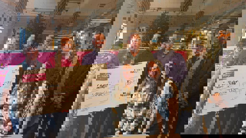 A group of nine people standing indoors in a modern office space, holding a large presentation cheque. The cheque reads “Candlelighters” and “From Yorkshire Housing” with an amount of £33,700.51 and a date of 31/3/26. Hanging lights, exposed ceiling beams, and plants are visible in the background.